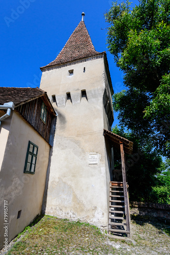 Large old white painted stone tower in the historical center of the Sighisoara citadel, in Transylvania (Transilvania) region of Romania, in a sunny summer day.