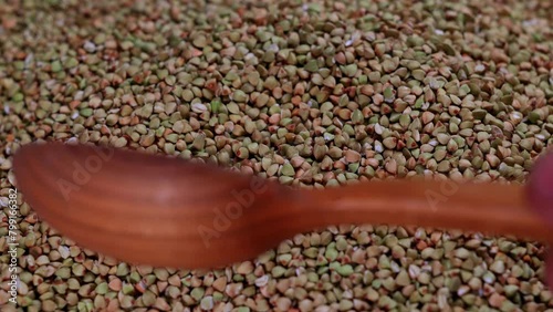 Grains of green buckwheat groats are turned over with a wooden spoon on a pile of buckwheat