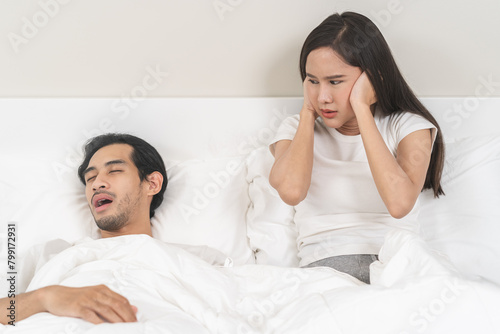 Snoring couple health asian man snore and sleeping at home while woman insomnia annoyed, bad noise cover ears with hand sleep problem apnea and relationship, wife looking at husband snoring in bed. © KMPZZZ