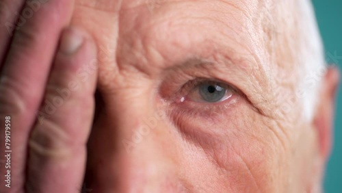 Close-up of an old man covering one eye with his hand