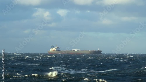 Vessel in storm. Waves with white foam. Sun illuminates tanker ship and waves