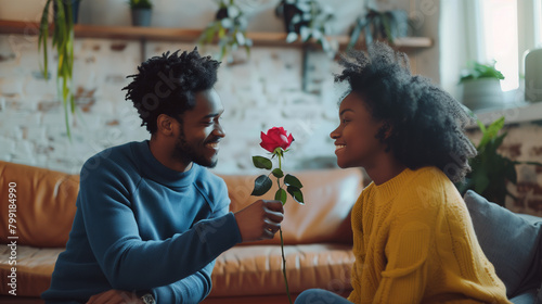 Young black man smilingly offers a rose to a delighted woman indoors photo