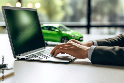 Man working on laptop in front of green car. Online buying and selling auto photo