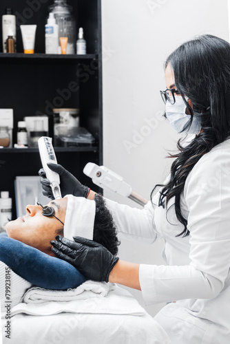 Hispanic female professional using a laser for skin care on a young Latin American man.