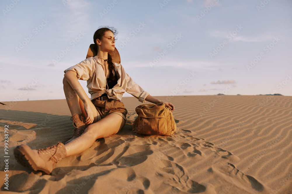 Woman Sitting on Sand in Desert with Hand on Shoulder and Bag, Peaceful Moment in Arid Landscape under Clear Sky Woman Sitting on Sand in Desert with Hand on Shoulder and Bag, Peaceful Moment in Arid Landscape under Clear Sky