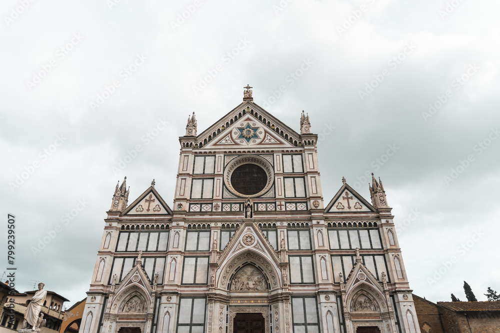 Basilica di Santa Croce's Neo-Gothic facade from Piazza di Santa Croce (Florence). Vibrant marble hues adorn three triangular pediments, echoing Florentine architectural tradition, under cloudy sky.