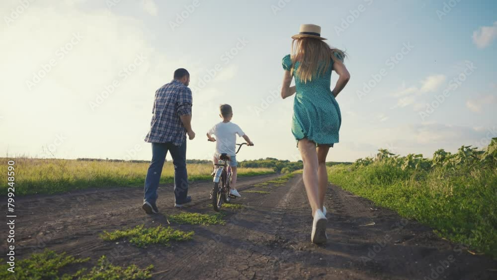 Mom dad teaching son ride bike together in village on summer vacation. Parents running near child boy father holding bicycle clapping hands supporting kid. Family weekend on nature, parents activity. Mom dad teaching son ride bike together in village on summer vacation. Parents running near child boy father holding bicycle clapping hands supporting kid. Family weekend on nature, parents activity.