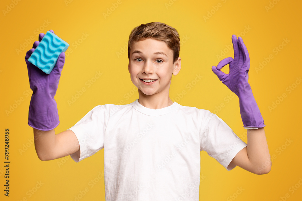 Cute boy in cleaning gloves showing OK sign and holding sponge Cute boy in cleaning gloves showing OK sign and holding sponge