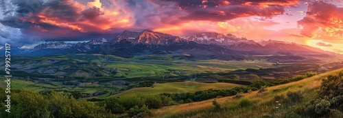 A majestic mountain range under the colorful sky, with rolling hills and green pastures in front of it