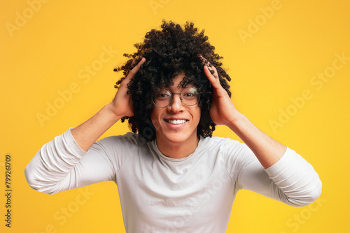 Surprised young curly-haired black guy clutching his head 