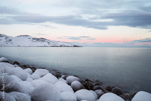 Coast Arctic ocean with boulders covered with ice and mountains on the horizon at sunset