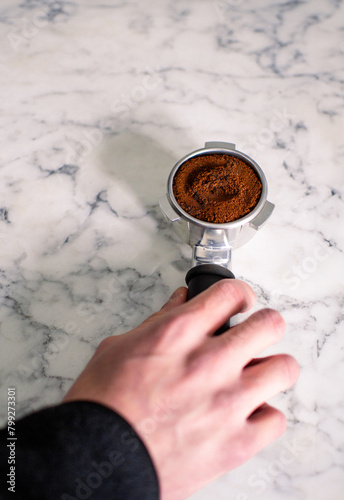 Barista preparing ground coffee in portafilter using tamper. Close-up top view of fresh coffee tablet. Portafilter with ground coffee, tamper on a concrete background with copy space. 