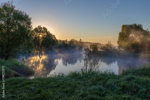Blue fog over the river, the rising sun reflected in the water, foggy morning in the countryside.