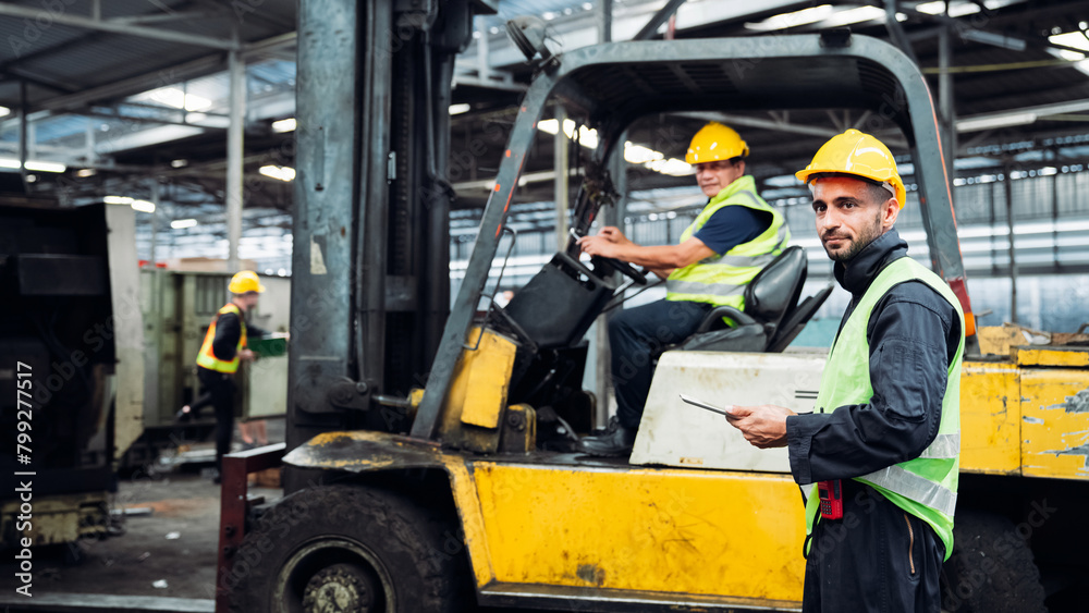 A man in a yellow and green safety vest stands in front of a forklift