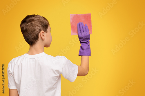 Teen boy washing wall with sponge  back view
