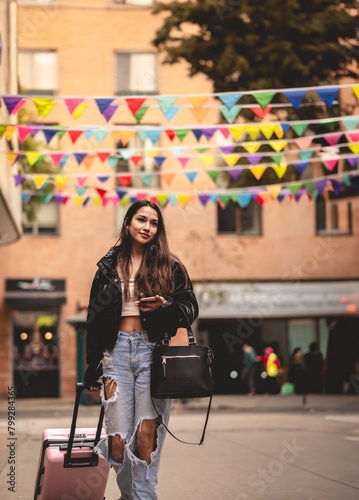 Stylish travel and urban exploration: vibrant young latina brunette with fashion look and pink suitcase exploring city downtown looking map on phone