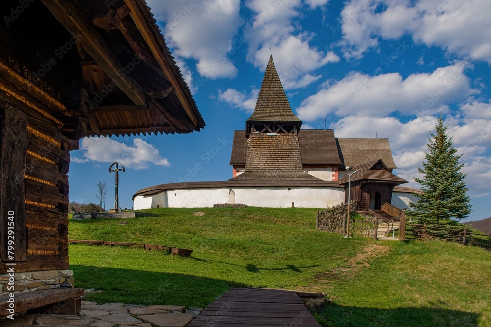 Old wooden historic fortified church, sunny day during early spring, blue sky with clouds. The village of Cerin near Banska Bystrica, Slovakia