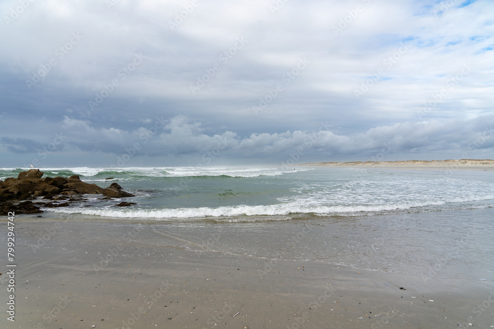 Sable mouillé, rochers, mer agitée sous un ciel couvert à la plage de la Torche en Bretagne, un tableau saisissant de la nature sauvage de la région.