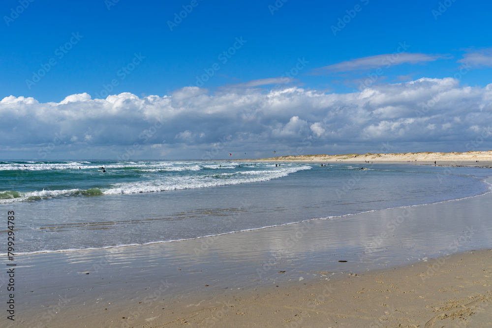 A la pointe de la Torche, dans le Finistère Sud, surfeurs et kitesurfeurs évoluent dans les eaux de Bretagne, sous les reflets des nuages sur le sable mouillé.