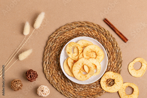 Sweet tasty apple chips in a white ceramic plate from above on a light beige background in rustic style. Healthy snack, top view.