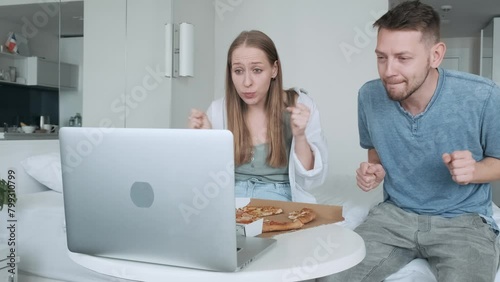 Young couple sport fans watching football match at home and cheering team. Overjoyed happy friends man and woman raising arms, celebrating goal and screaming while watching soccer game with pizza photo