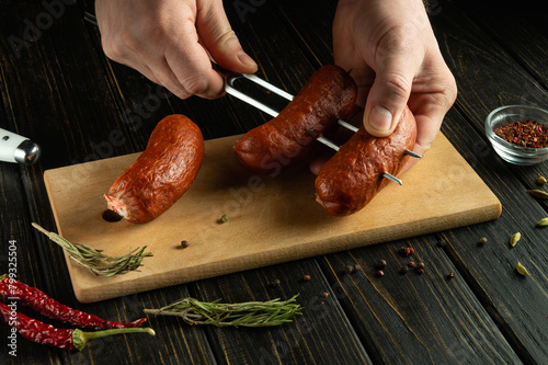The concept of cooking sausages on the grill. A fork with Munich sausages in the hands of a cook on the kitchen table.