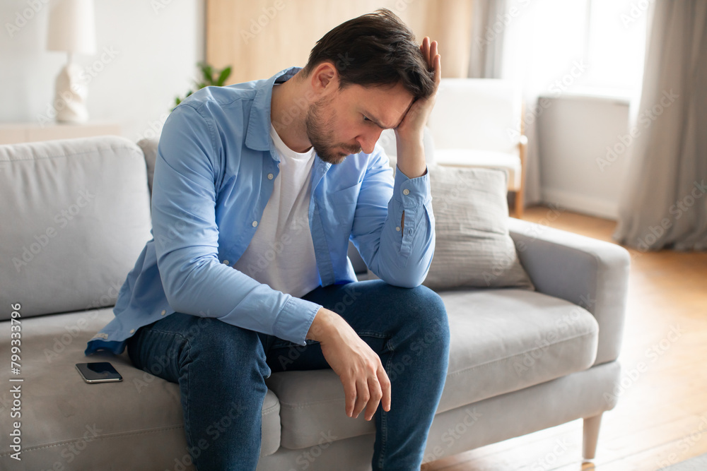 Man Sitting on Couch Holding Head, Home Interior Man Sitting on Couch Holding Head, Home Interior