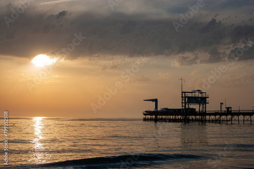 Crane on the sea pier in the rays of the setting sun. Silhouette of a pier on the sea horizon. Evening at sea on a cloudy day