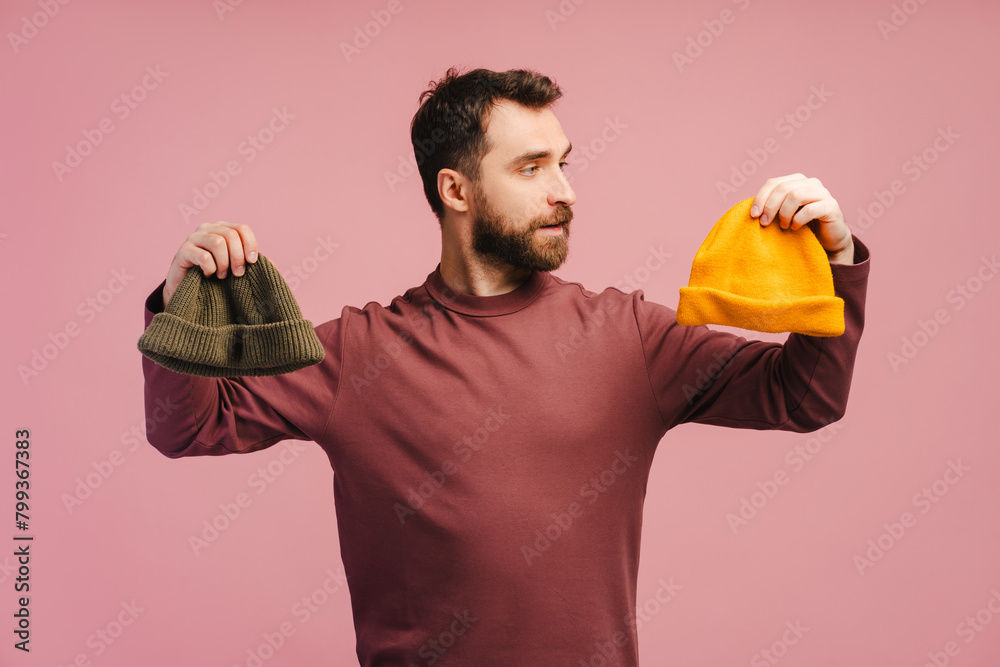 Amazed middle aged caucasian bearded man 40s, holding two hats, choosing Amazed middle aged caucasian bearded man 40s, holding two hats, choosing