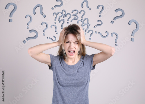 Amnesia. Stressed young woman and question marks on light background