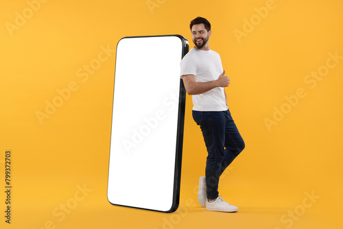 Man standing near huge mobile phone with empty screen on dark beige background. Mockup for design
