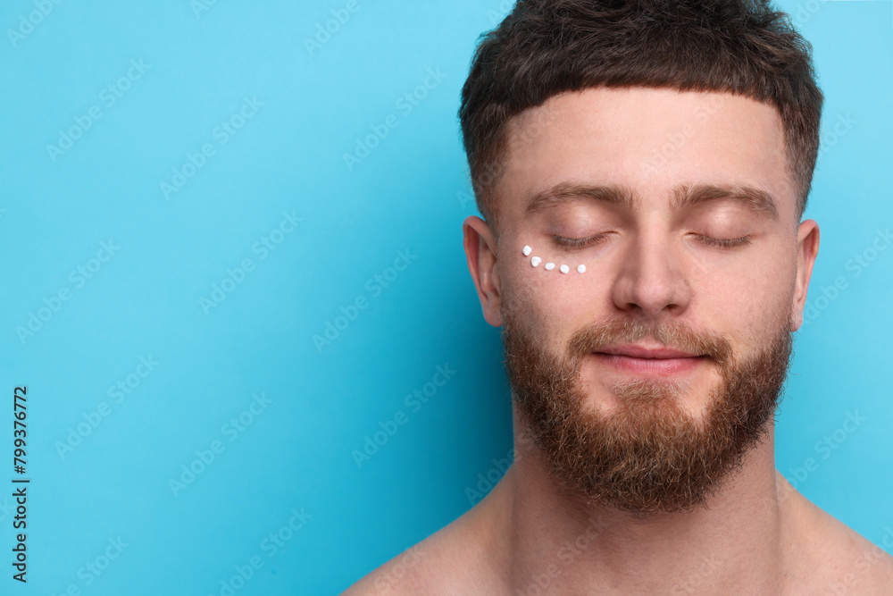 Obraz premium Handsome man with moisturizing cream on his face against light blue background, space for text