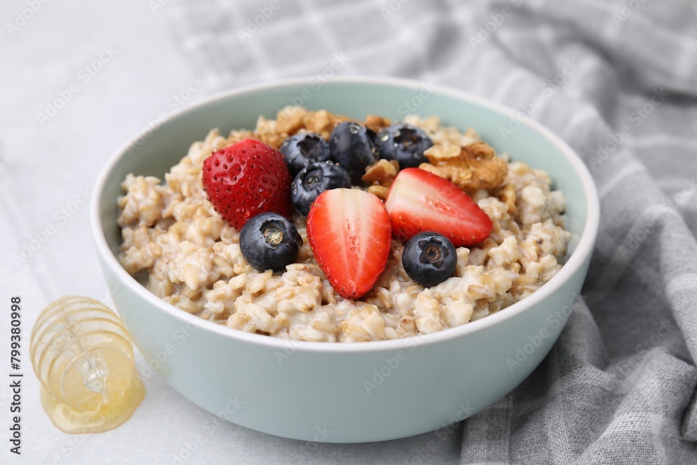 Tasty oatmeal with strawberries, blueberries and walnuts in bowl on grey table Tasty oatmeal with strawberries, blueberries and walnuts in bowl on grey table