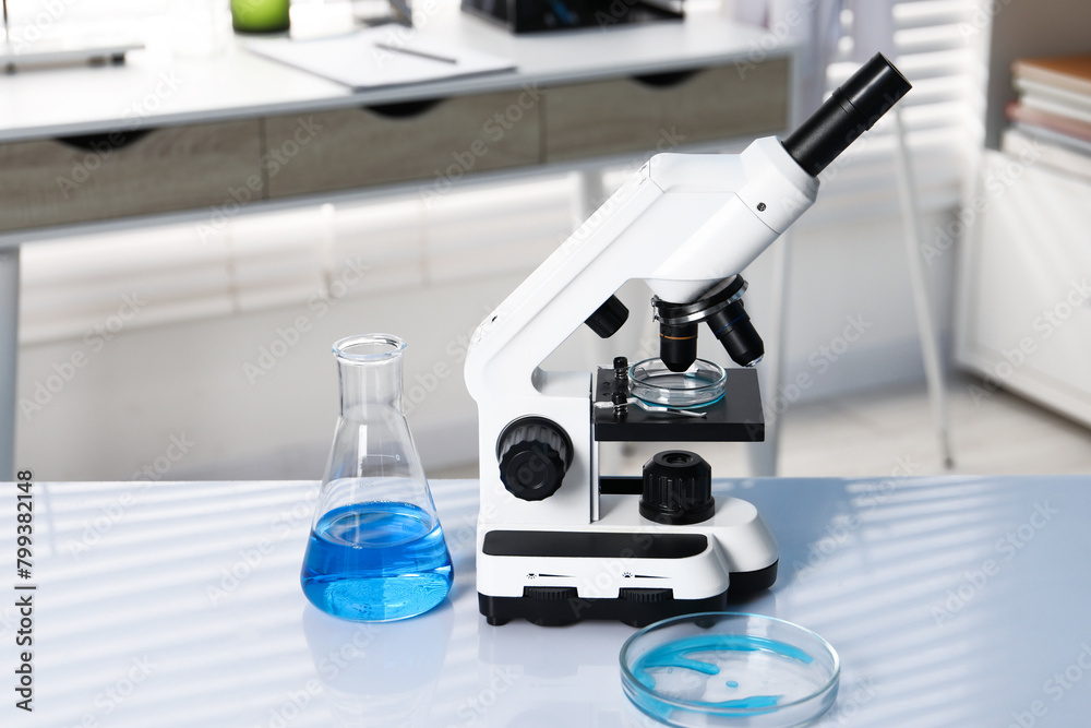 Laboratory analysis. Flask with blue liquid, petri dish and microscope on white table indoors Laboratory analysis. Flask with blue liquid, petri dish and microscope on white table indoors