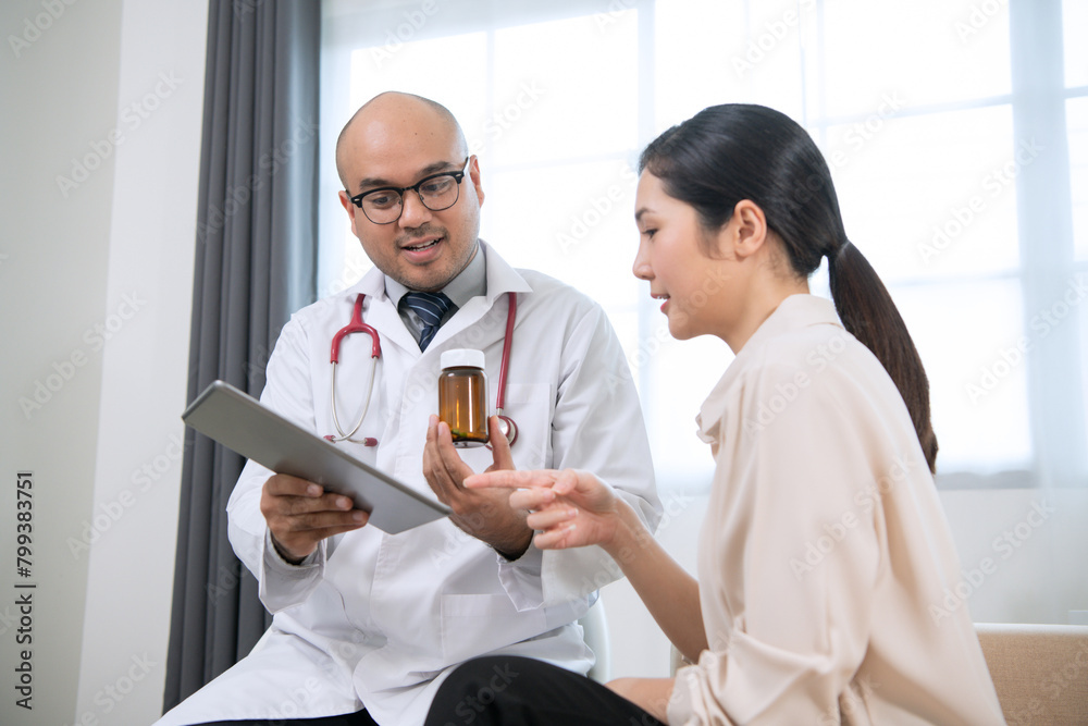 Fototapeta premium Foreign tanned male doctor in white medical clothes discussing woman's illness male doctor opens an iPad, shows treatment and medication information, and provides information of each drug.