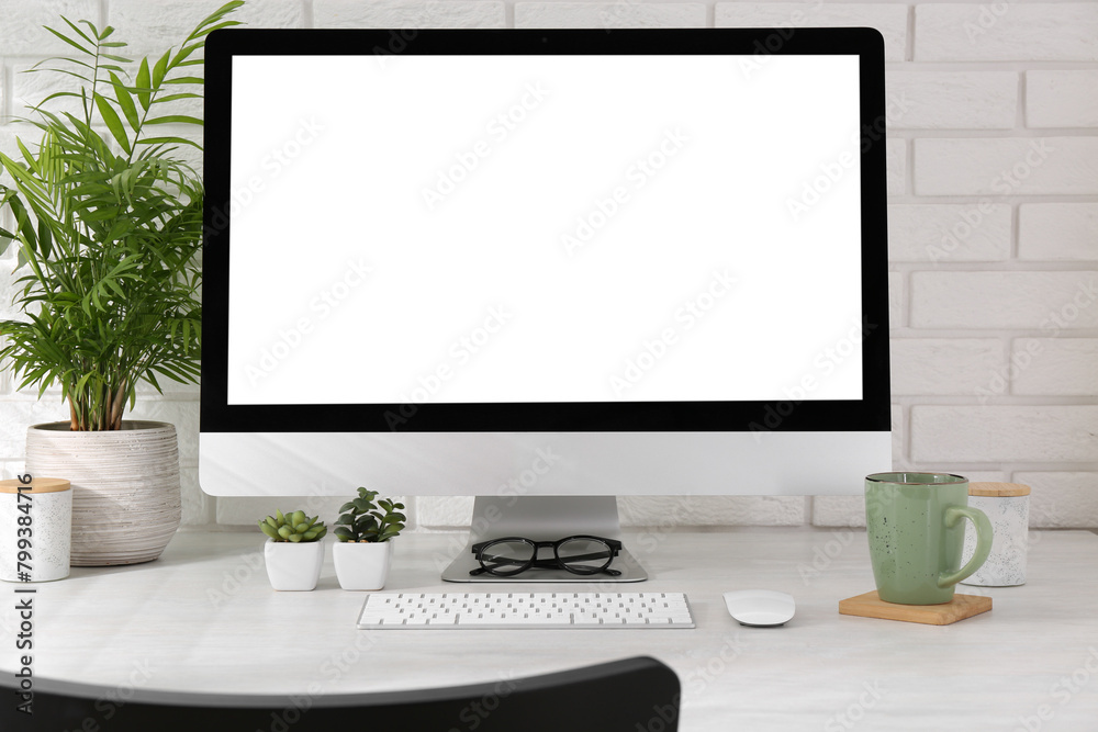 Fototapeta premium Office workplace with computer, glasses, cup and houseplants on light table near white brick wall