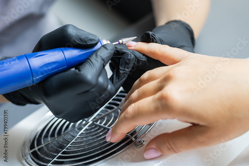 Bild auf Leinwand Female master using electric nail file while doing manicure for client in beauty