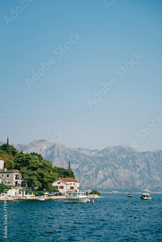 Boats stand off the coast of Perast with old houses among green trees. Montenegro