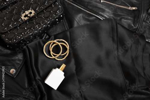 Leather bag, bottle of perfume and golden bracelets on black fabric, flat lay. Space for text