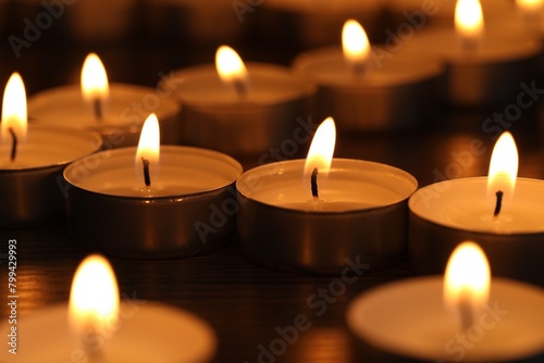 Burning tealight candles on dark surface, closeup