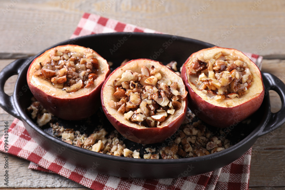 Tasty baked apples with nuts and honey in baking dish on wooden table, closeup Tasty baked apples with nuts and honey in baking dish on wooden table, closeup