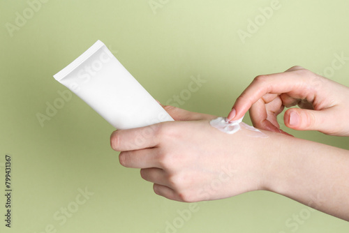 Woman with tube applying cream on her hand against green background, closeup