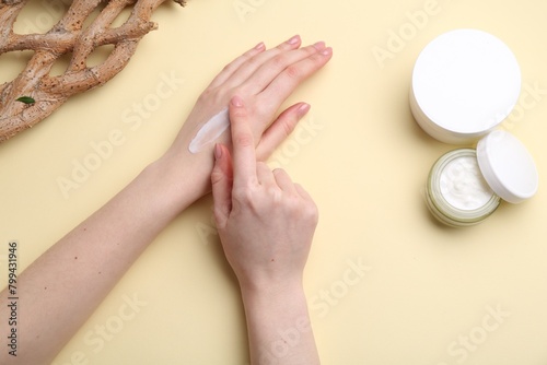 Woman applying hand cream on beige background, top view