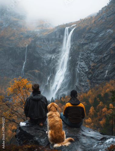 Two people and a dog sitting by a majestic waterfall in autumn © CamiloA