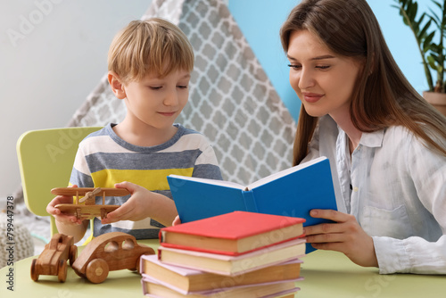 Mother and her son with different books sitting at table in children's room