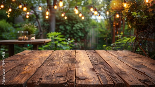 A rustic wooden table in a garden setting is warmly lit by festive lights  with a golden sunset peeking through the trees..