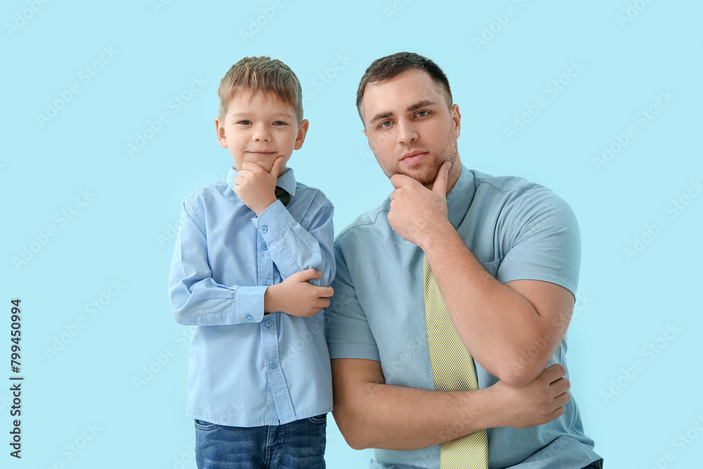 Thoughtful father and his little son on blue background Thoughtful father and his little son on blue background