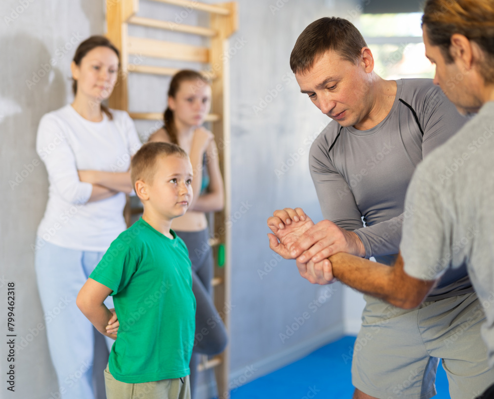 Obraz premium In gym at self-defense training, trainer on man explains technique of palm grip, boy, girl and woman are trained