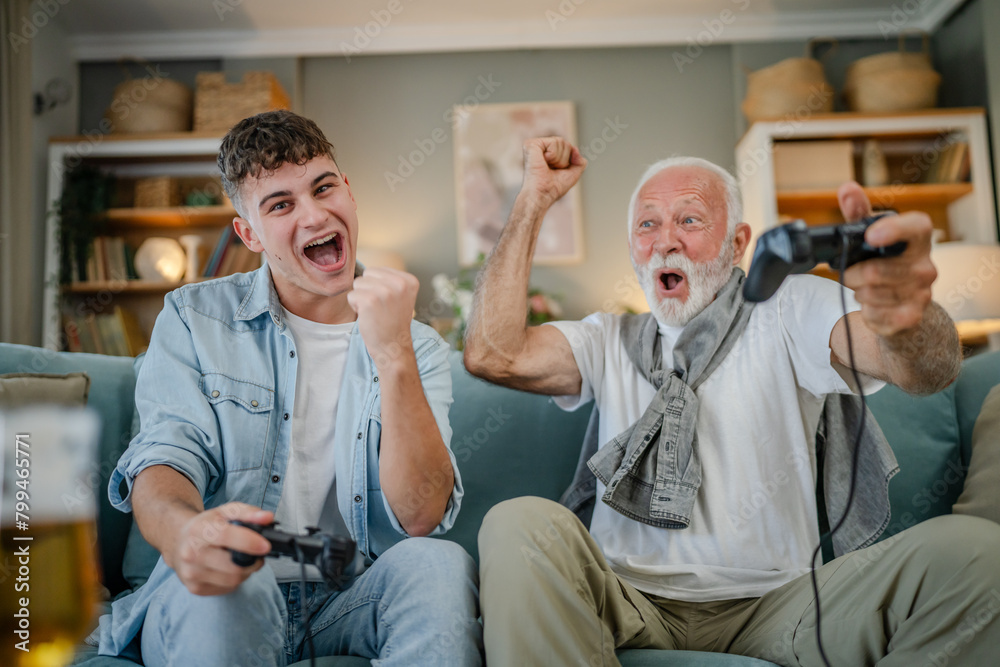 Obraz premium teenager male and his grandfather senior man play console video game