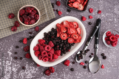Bowls with different freeze-dried berries and spoons on grey background photo